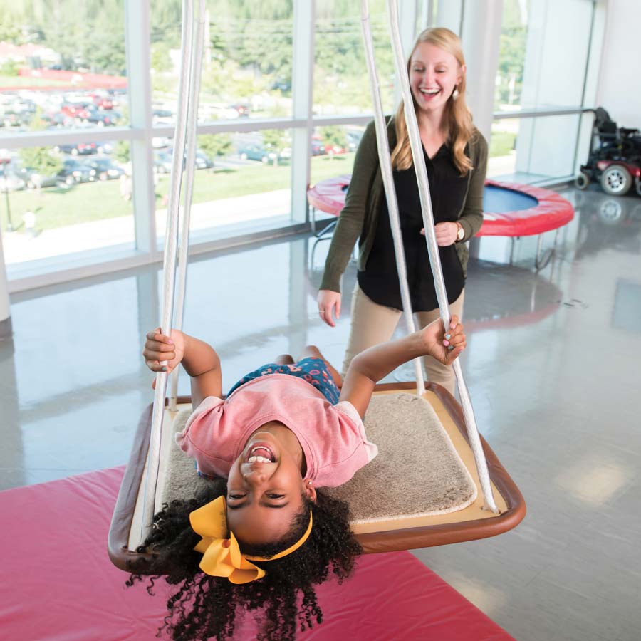 HowtoApply-OTAPrograms_Feature3 Occupational therapist pushes client in wheelchair on playground